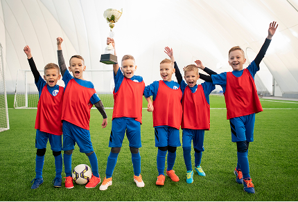 Kinderfußballmannschaft jubelt mit einem Pokal auf dem Spielfeld