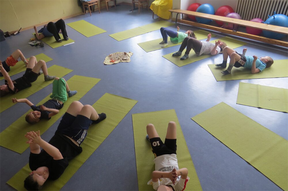 Kinder machen gemeinsam Yoga auf Matten in der Turnhalle