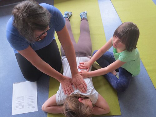 Yogalehrerin unterstützt ein Kind bei einer Übung auf der Matte