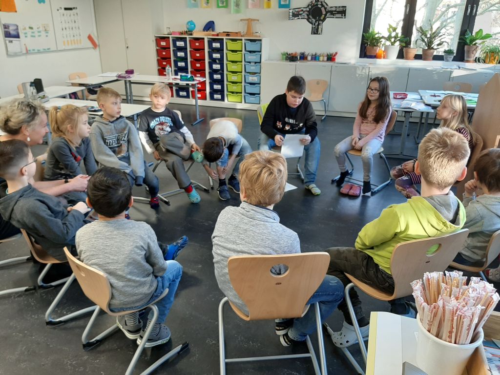 Kinder lesen gemeinsam im Stuhlkreis im Klassenraum